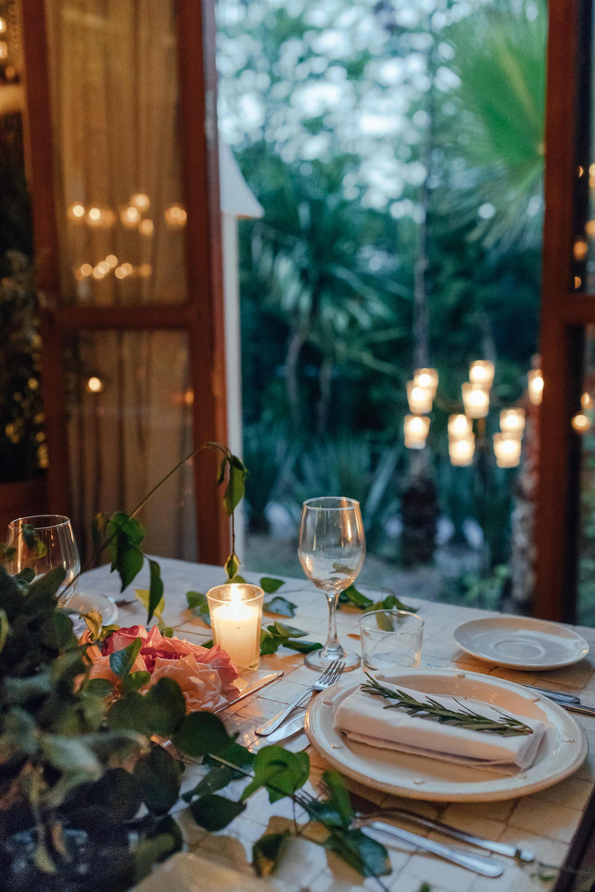 a table set for a formal dinner with candles and greenery