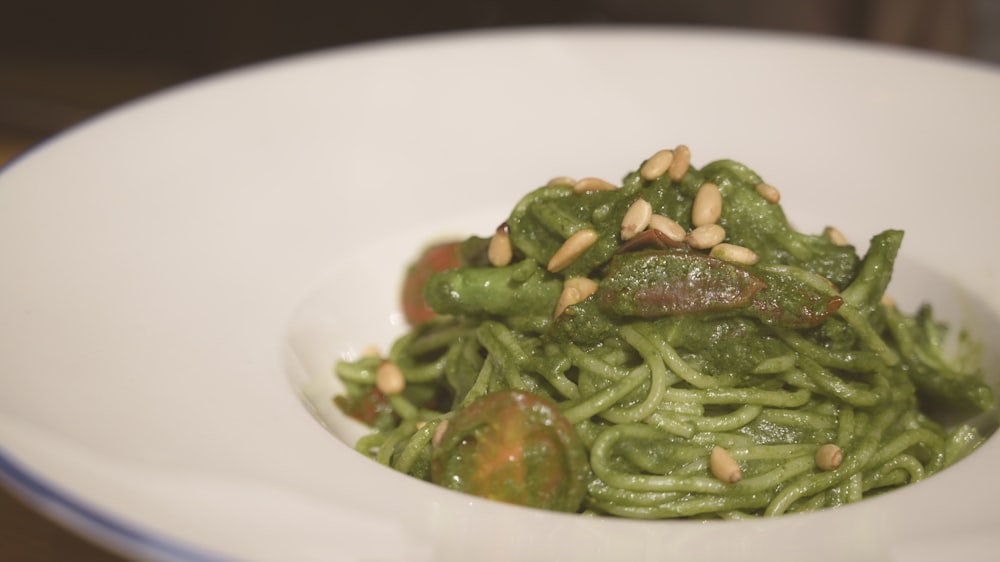 a white bowl filled with green pasta covered in pesto