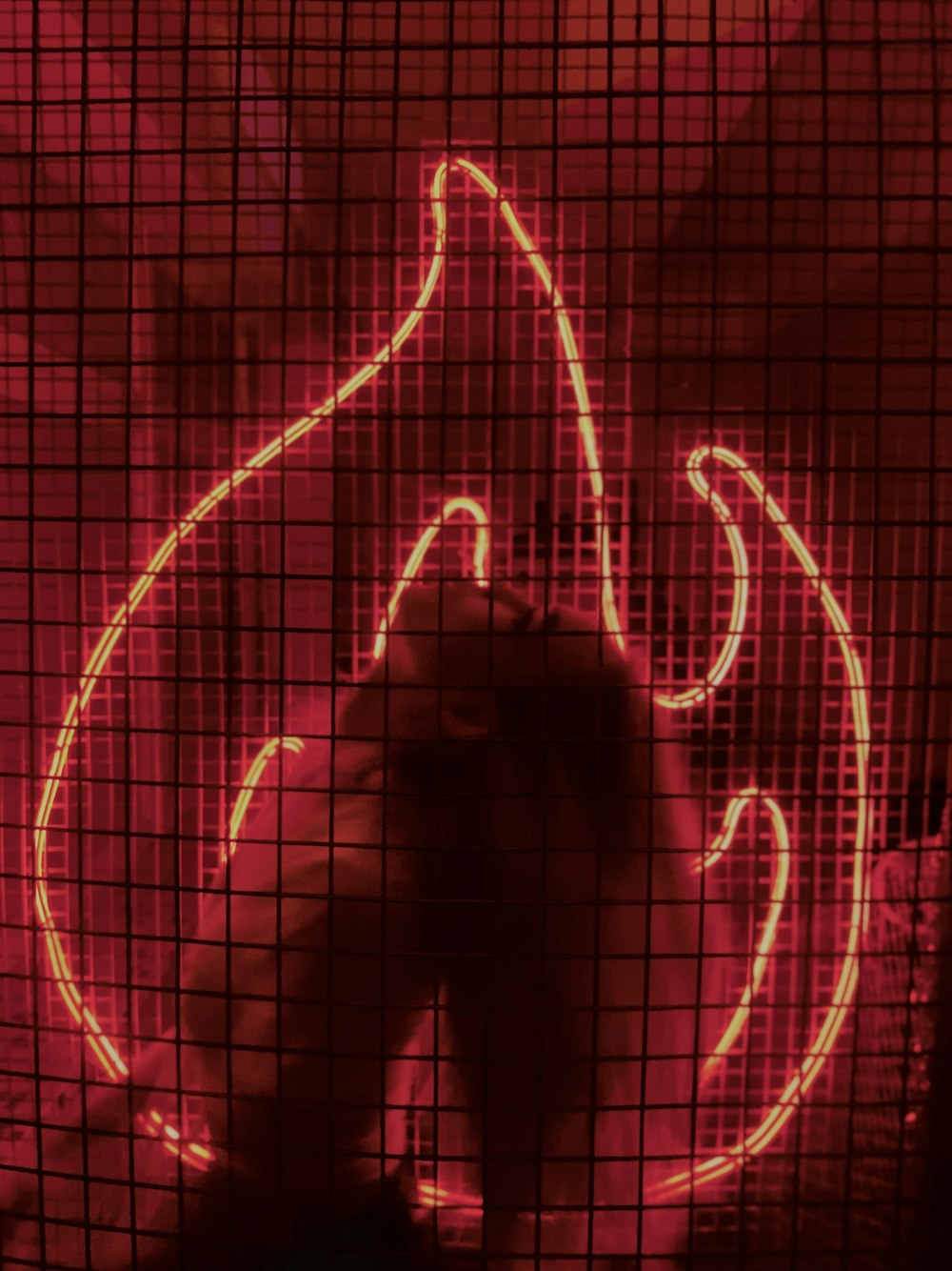 a red neon sign behind a wire mesh fence