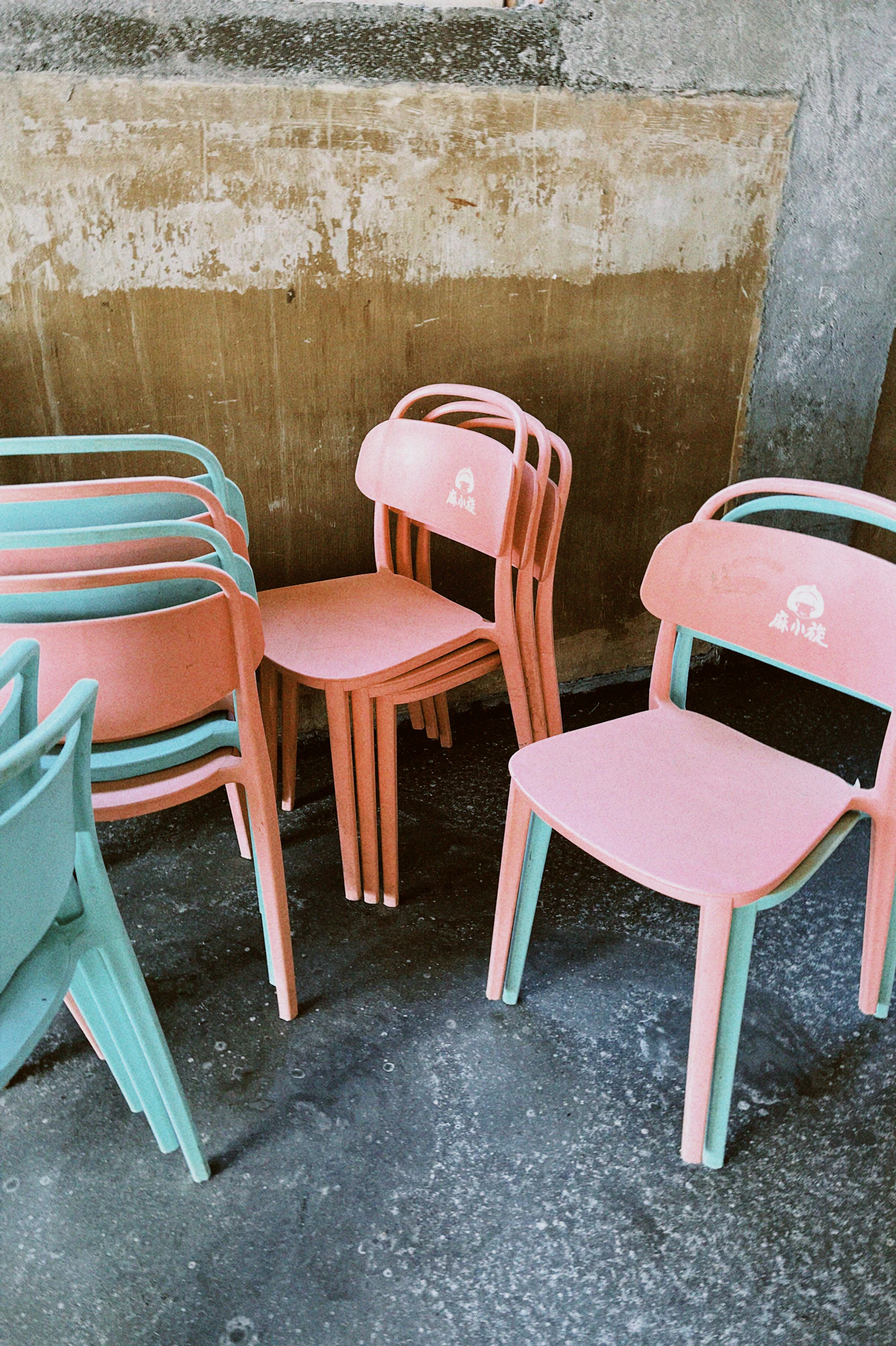 Pink and mint children's chairs stacked against a concrete wall