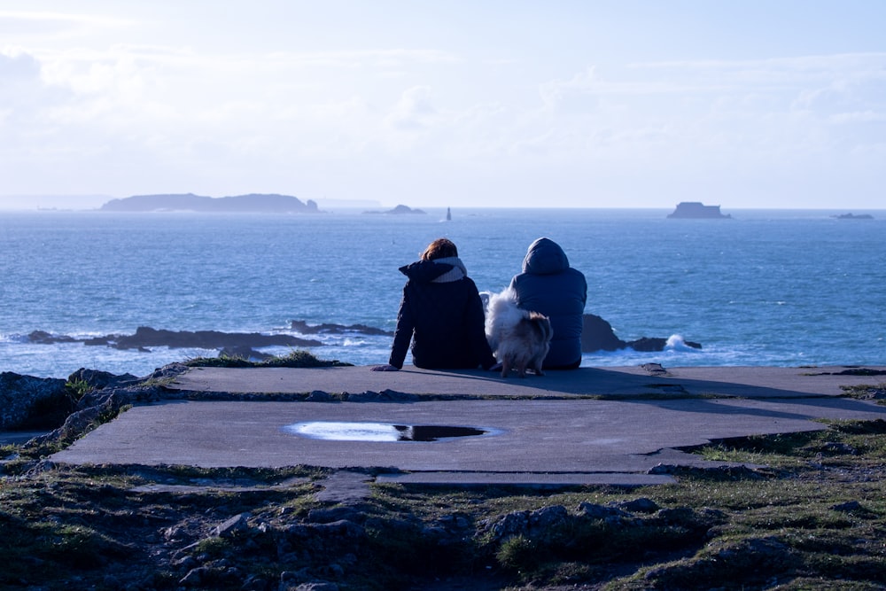 two people sitting on a rock overlooking the ocean