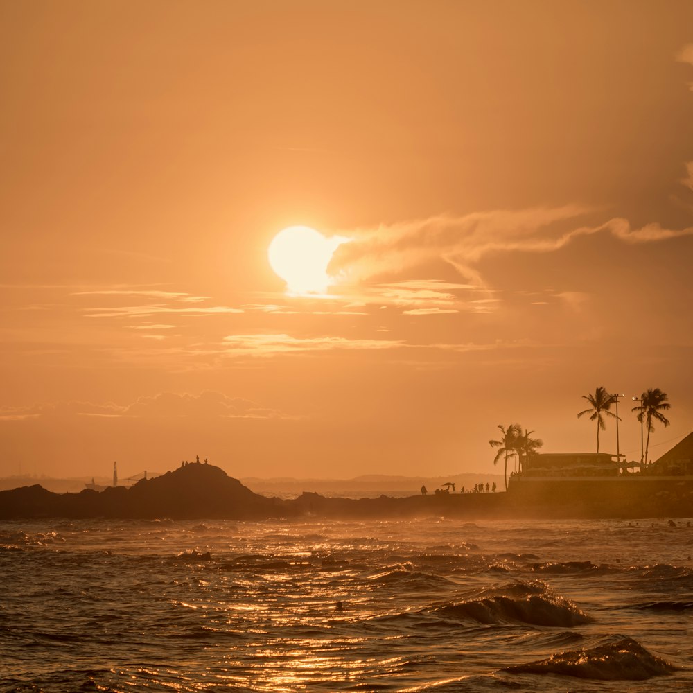 the sun is setting over the ocean with a small island in the distance