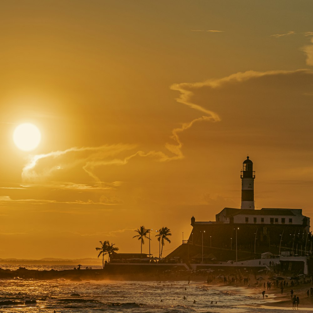 the sun is setting over a beach with a lighthouse