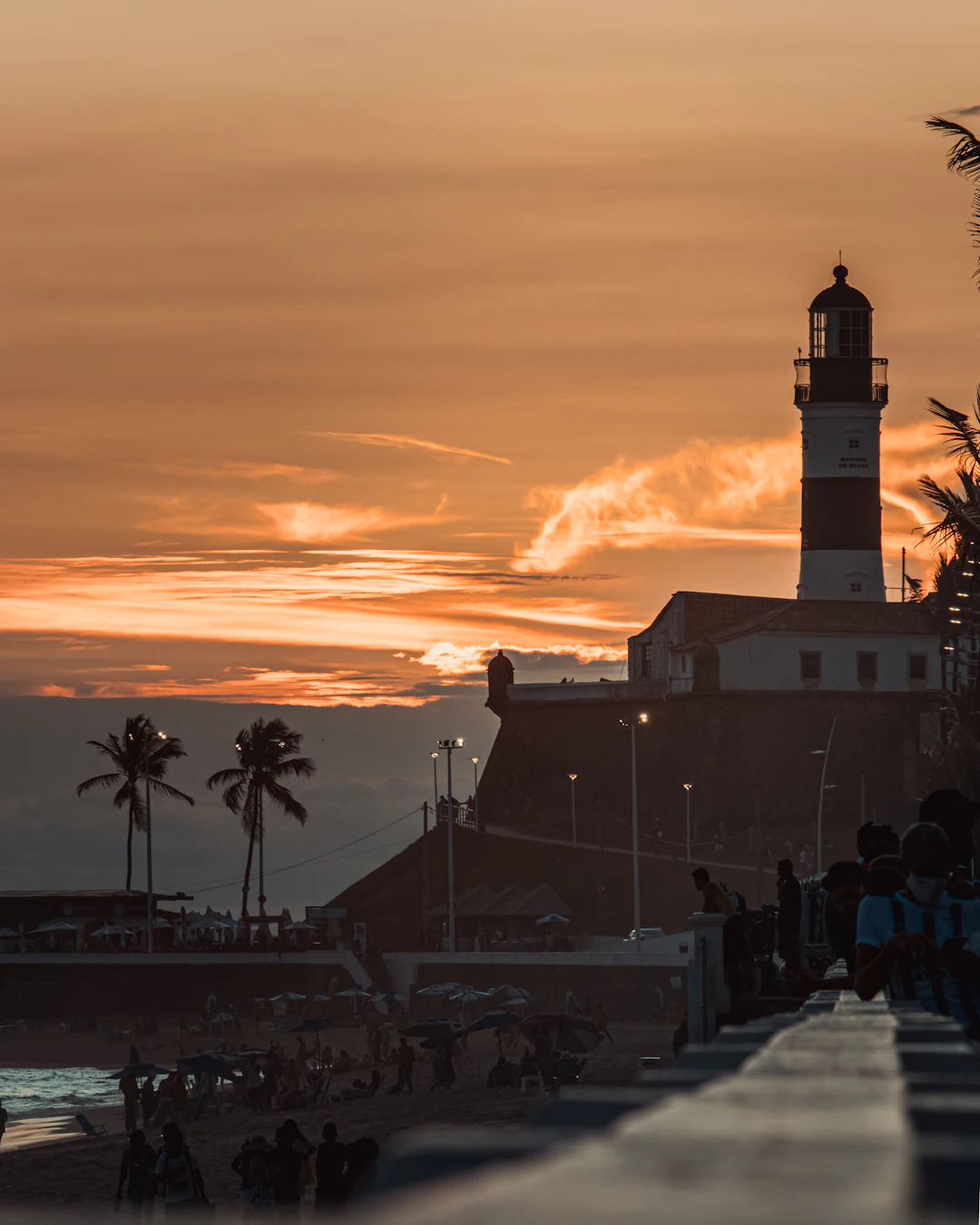 Lighthouse by the sea at sunset, with people walking along the shore