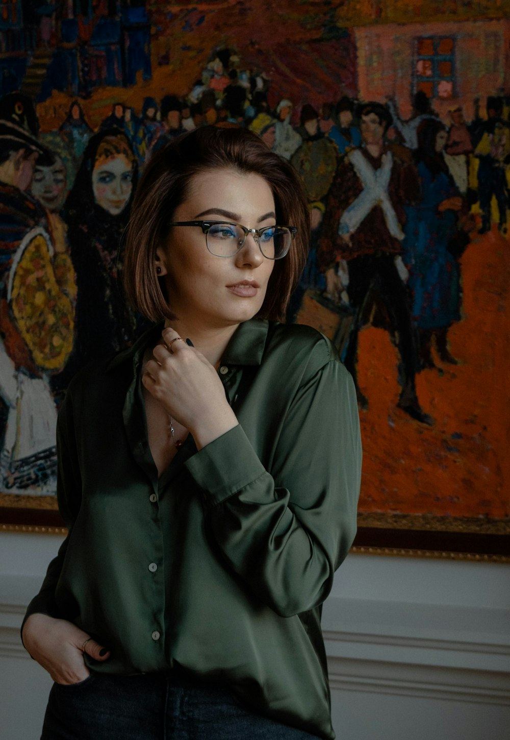 a woman wearing glasses standing in front of a painting