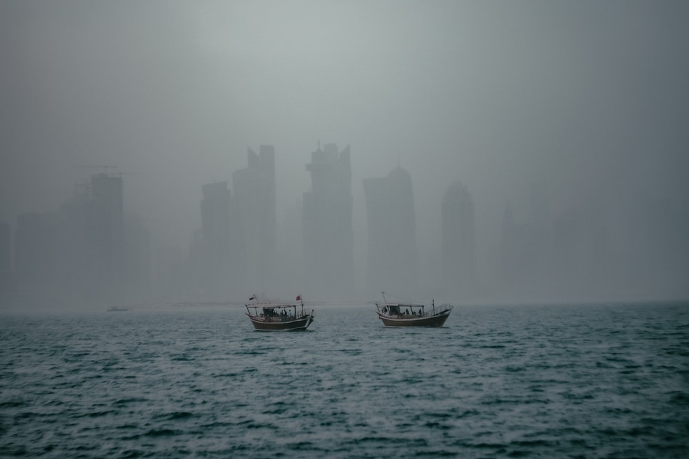 two boats floating in the ocean on a foggy day