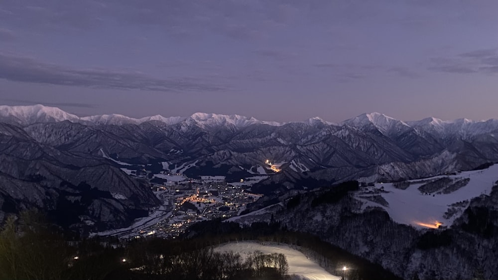 a night view of a snowy mountain with a city in the distance