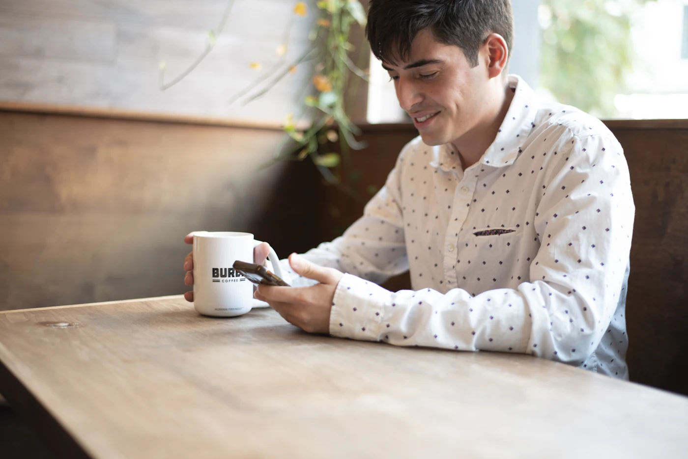Hombre sentado a una mesa con café mirando el móvil