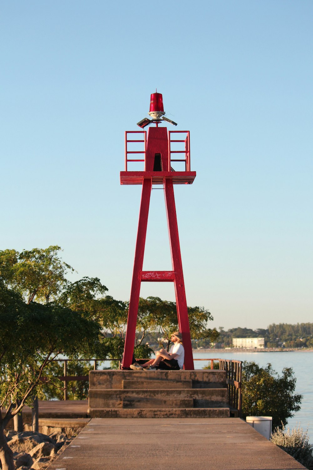 um homem sentado em uma torre vermelha ao lado de um corpo de água