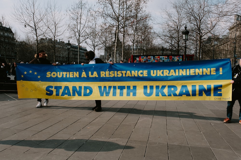 a group of people holding a banner that says stand with ukraine