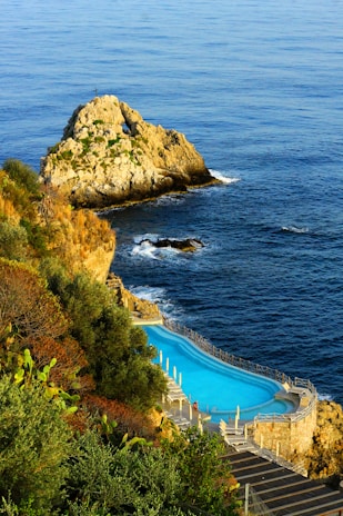 a swimming pool on the side of a cliff next to the ocean
