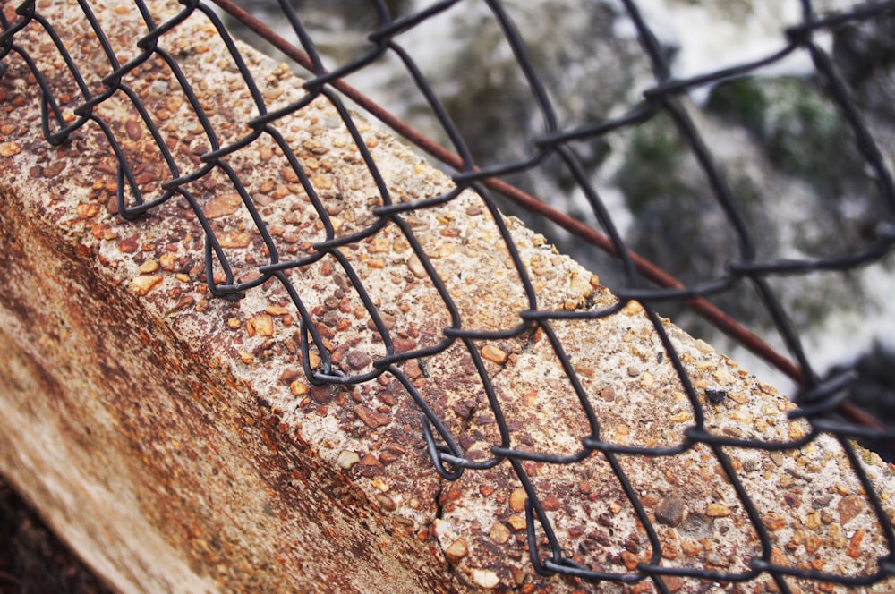 a close up of a fence with rocks and a river in the background