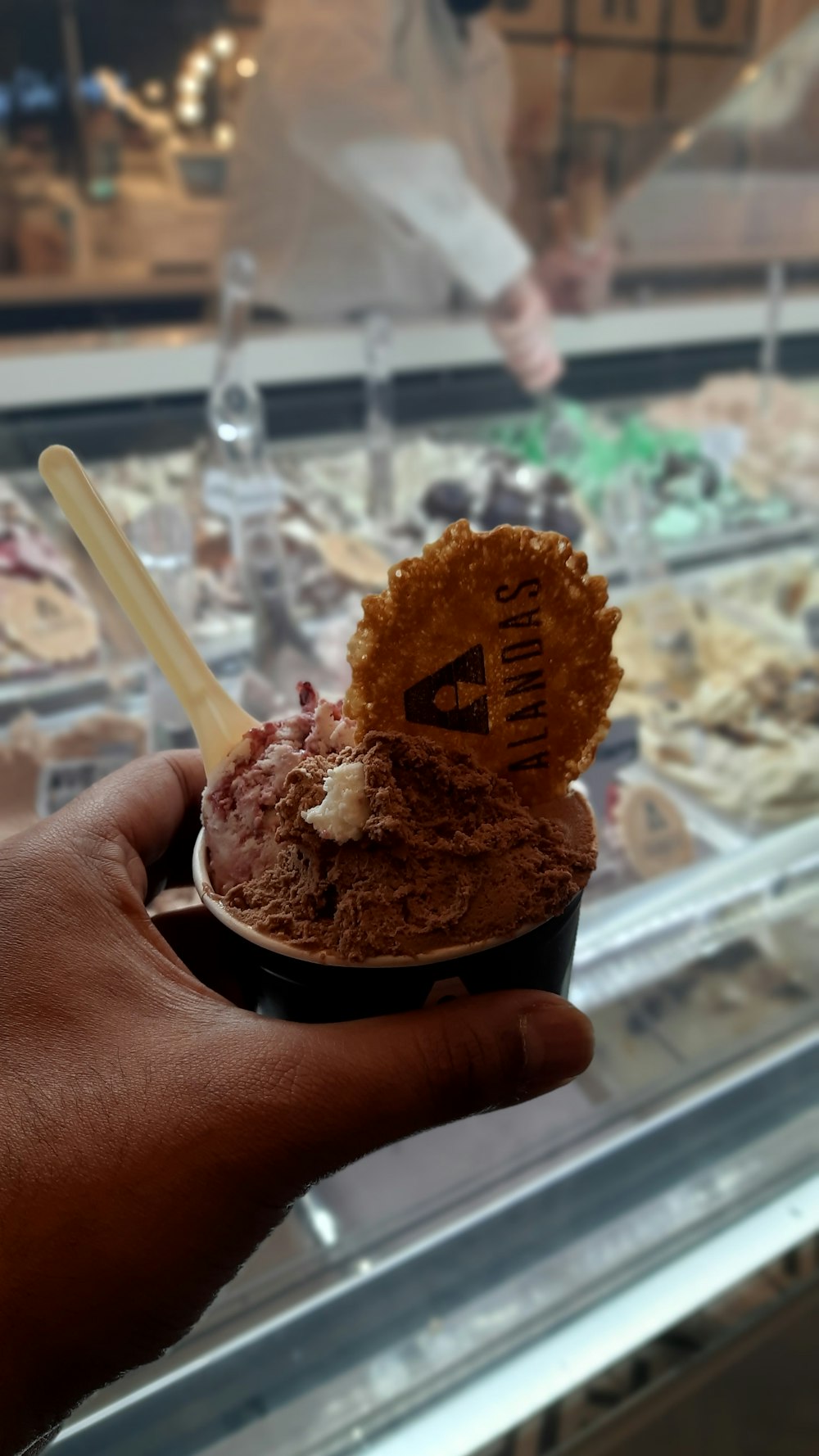 a person holding a cup of ice cream in front of a display case