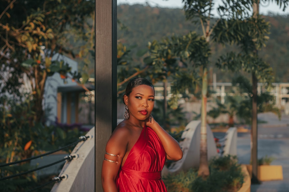 a woman in a red dress leaning against a pole