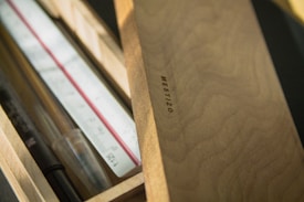 A wooden box partially open, displaying a ruler, a pen, and a clear pencil. The box is made of light wood, displaying a grain texture, and has 'MESTIZO' embossed on the lid.