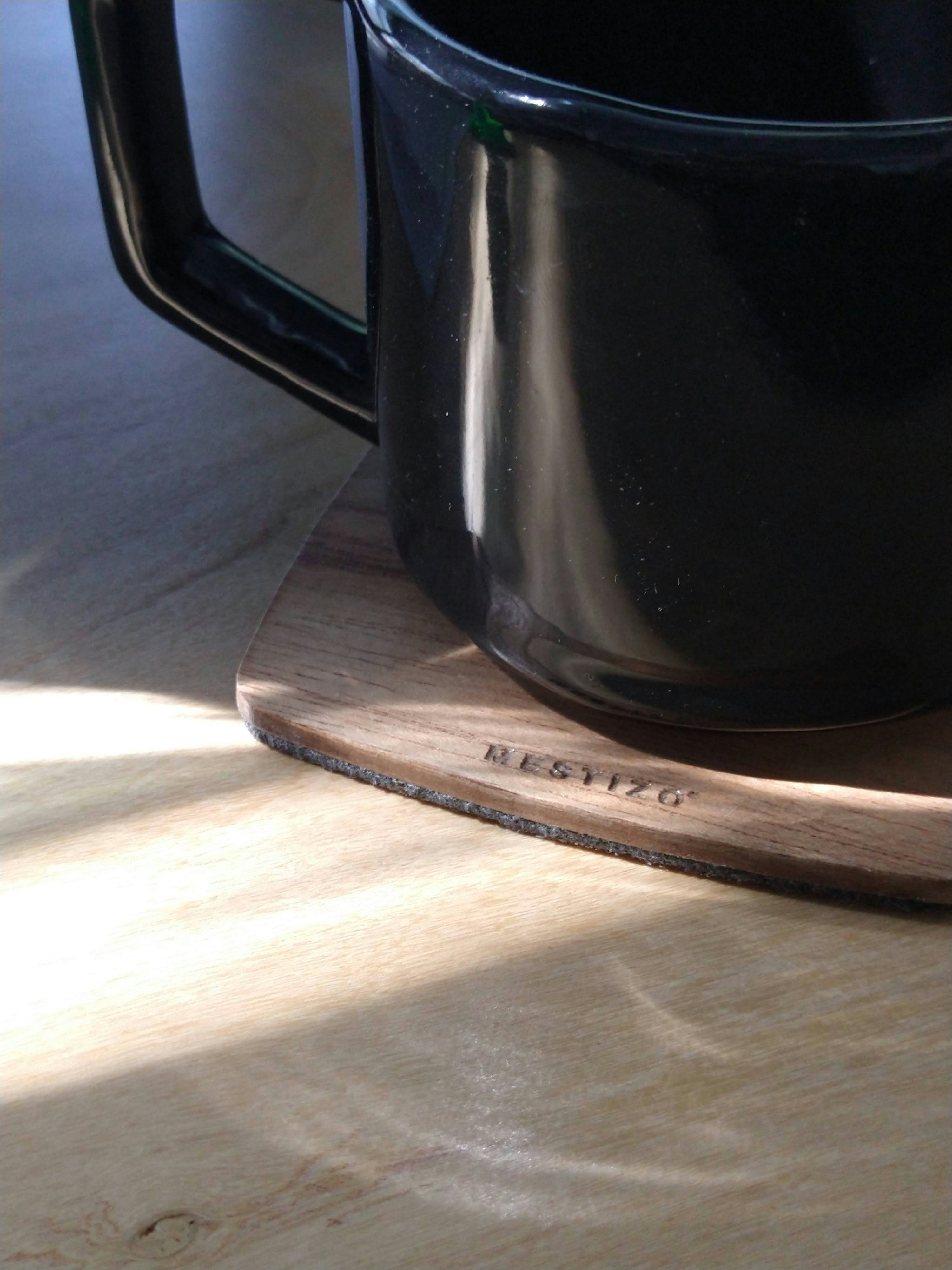 a black coffee mug sitting on top of a wooden coaster