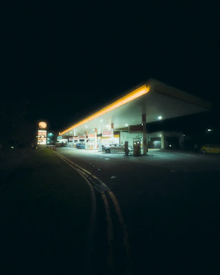 A bright gas station canopy glowing under the evening sky with cars fueling up.