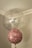 Two balloons are floating indoors, one large and transparent with multicolored confetti inside, and one smaller pink balloon with the words 'Happy Birthday' written on it in a stylish script. The setting is a corner of a room with muted colors and a simple ceiling molding.