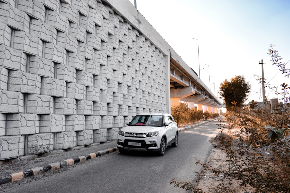 a white car driving down a road next to a wall
