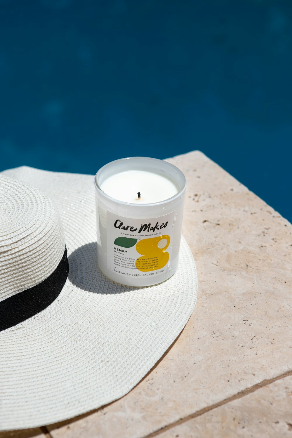 a white hat sitting next to a candle near a pool