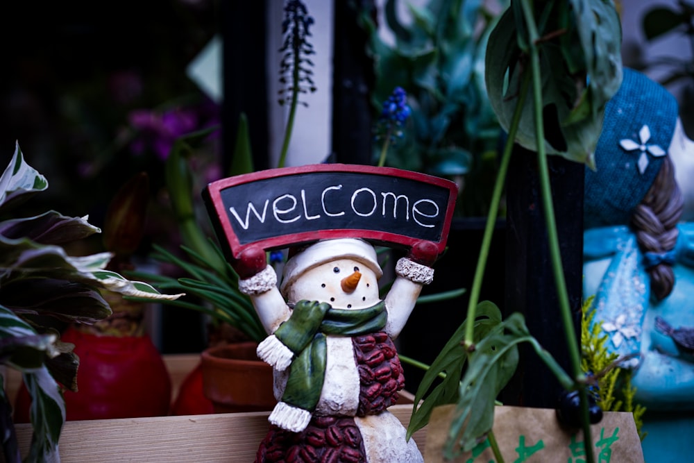 a small snowman holding a welcome sign