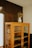 A vintage wooden cabinet with glass-paneled doors stands against a dark wall. On top of the cabinet, there is an old metal pitcher filled with dried flowers, adding a rustic touch. The cabinet is empty, displaying its wooden shelves.