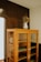 A vintage wooden cabinet with glass-paneled doors stands against a dark wall. On top of the cabinet, there is an old metal pitcher filled with dried flowers, adding a rustic touch. The cabinet is empty, displaying its wooden shelves.
