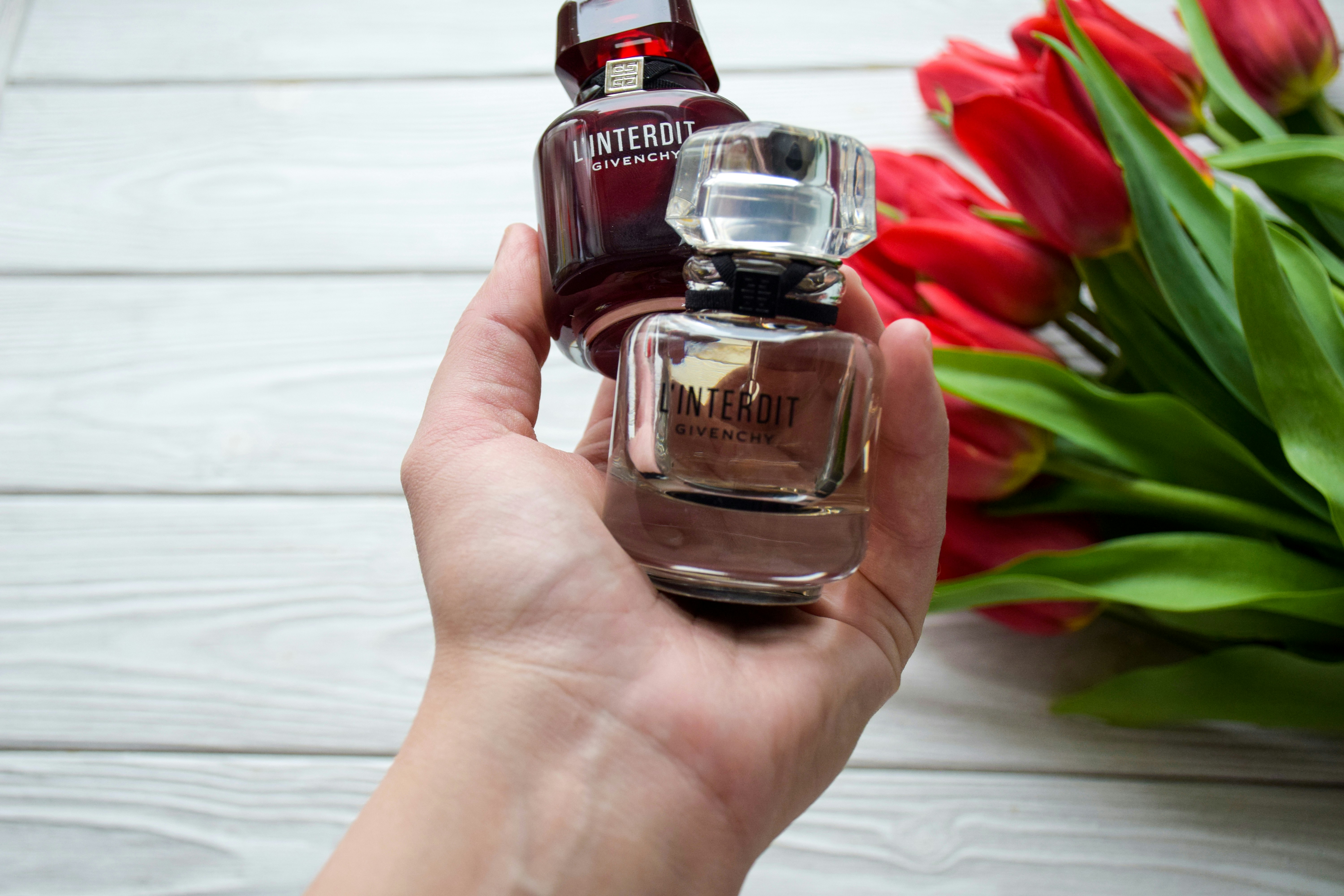 a person holding a bottle of perfume next to a bouquet of flowers