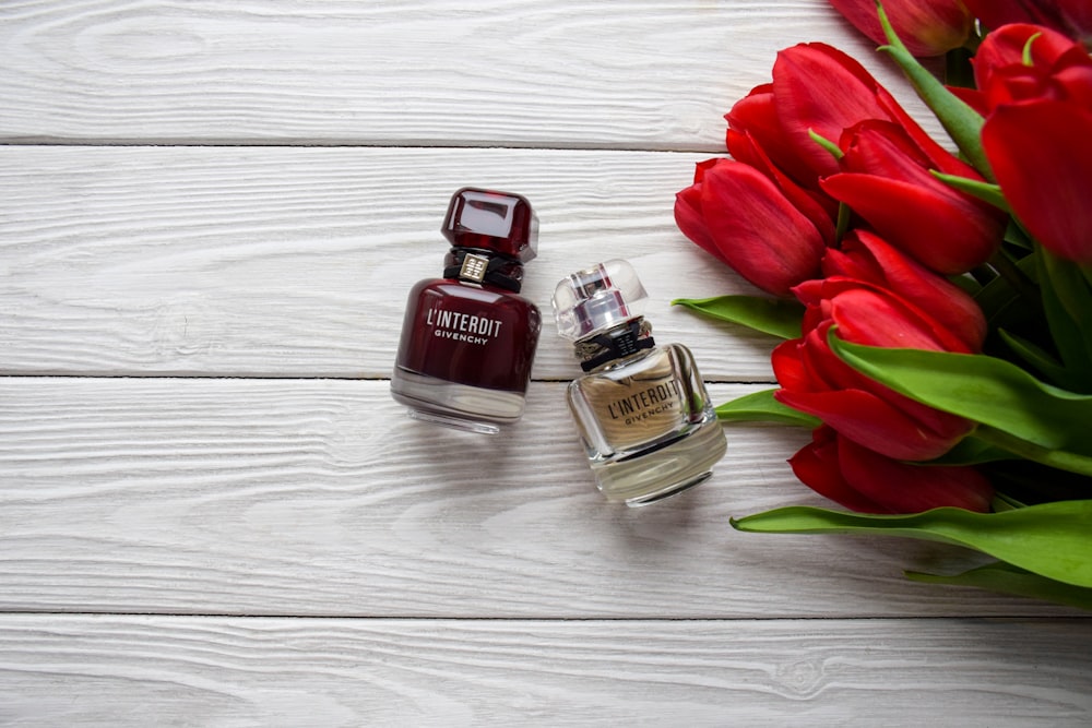 a bouquet of red tulips next to a bottle of perfume