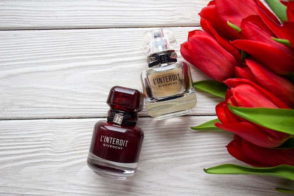 a bottle of perfume next to a bouquet of red tulips