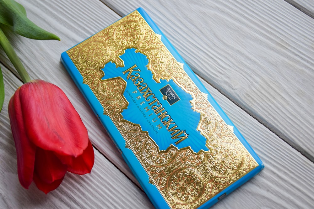 a red tulip sitting next to a blue and gold book