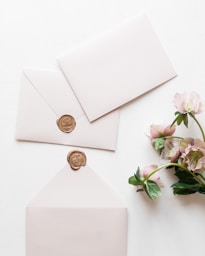 a white envelope with a wax stamp and some pink flowers