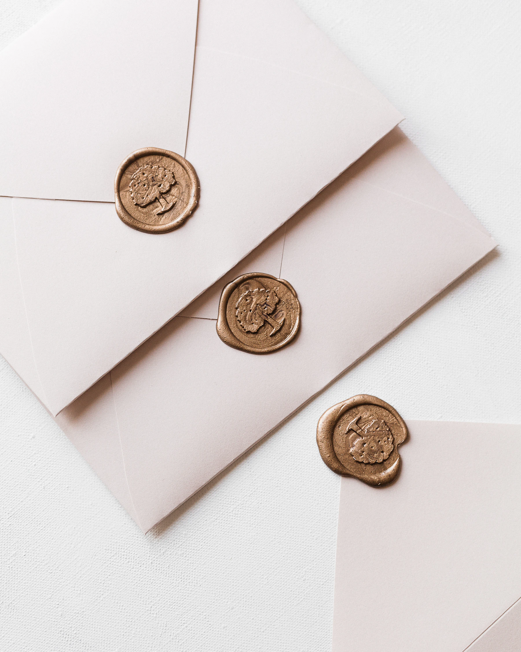 Three blush envelopes closed with gold wax seals