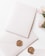 A blank white envelope and matching card are adorned with a gold wax seal featuring an intricate design. Nearby, a small bouquet of light pink flowers adds a delicate touch, contrasting with the soft white background.