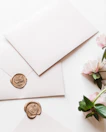a white envelope with a wax stamp and some pink flowers