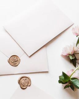 a white envelope with a wax stamp and some pink flowers