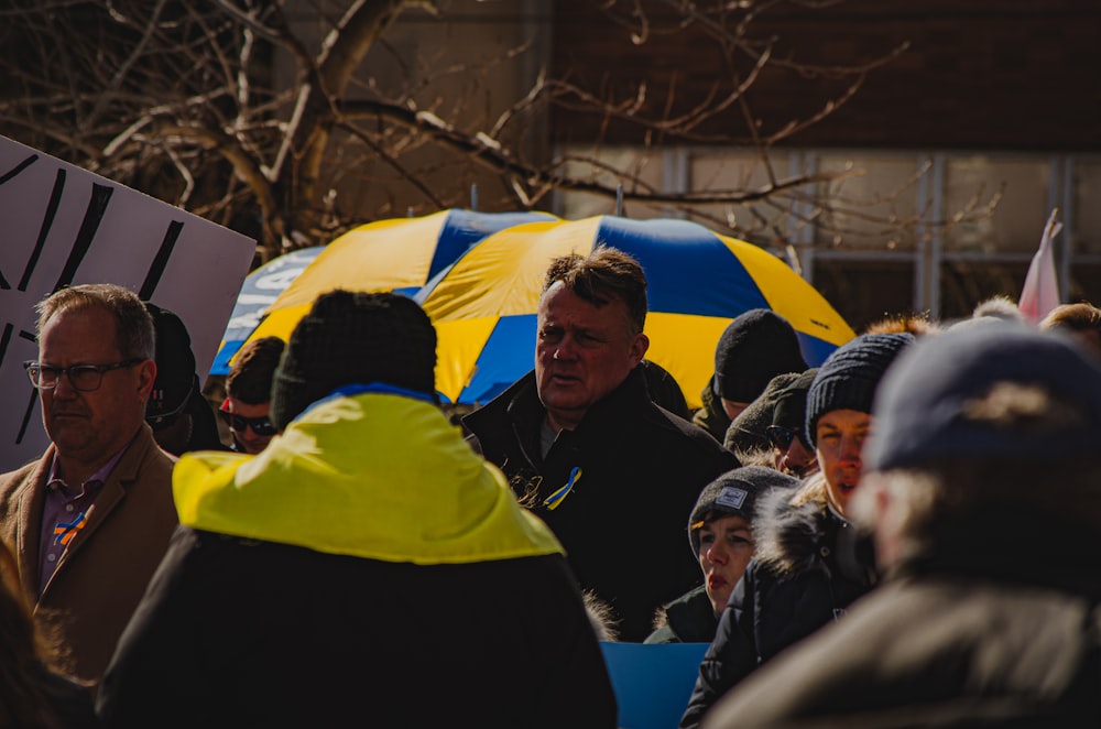 a crowd of people standing around a yellow and blue umbrella