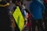 A person stands holding a bright yellow poster listing various years and places, possibly signifying historical or political events. The poster includes years like 1992, 1994, 1999, 2008, 2014, 2015, 2022, and 2023, and mentions locations such as Moldova, Chechnya, Georgia, Ukraine, Syria, and ends with the phrase 'STOP PUTIN'. Several people are gathered around, some dressed in blue and yellow, and a microphone is visible in the foreground, suggesting a protest or interview setting.