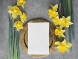 a plate with a blank paper on it next to yellow flowers
