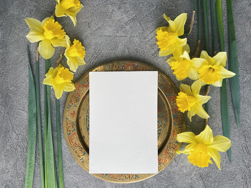 a plate with a blank paper on it next to yellow flowers