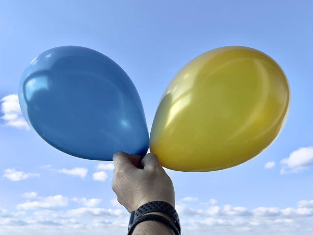 a hand holding a blue and a yellow balloon
