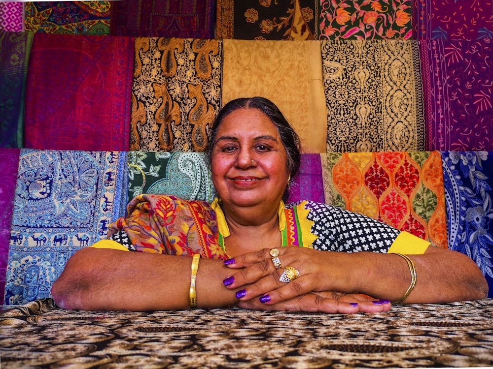a woman sitting in front of a display of colorful fabrics