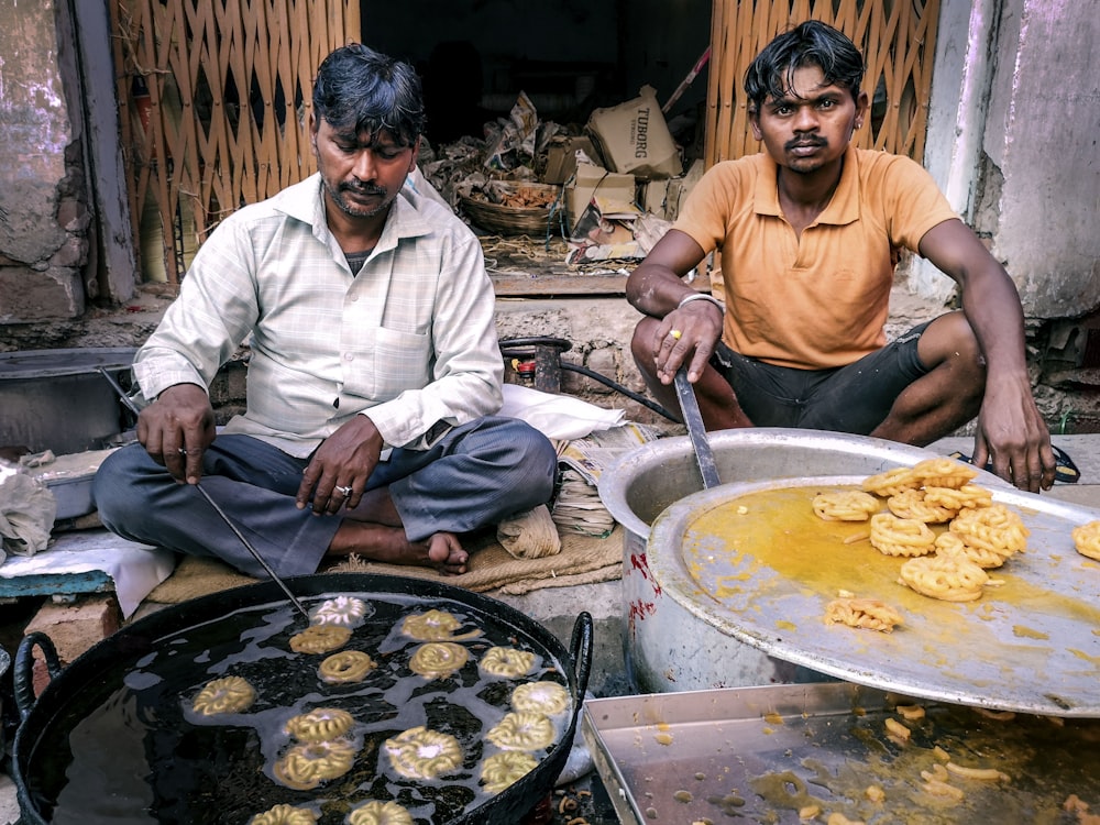 two men sitting on the ground with food in front of them