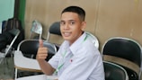 a young man sitting at a table giving a thumbs up