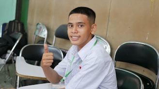 a young man sitting at a table giving a thumbs up