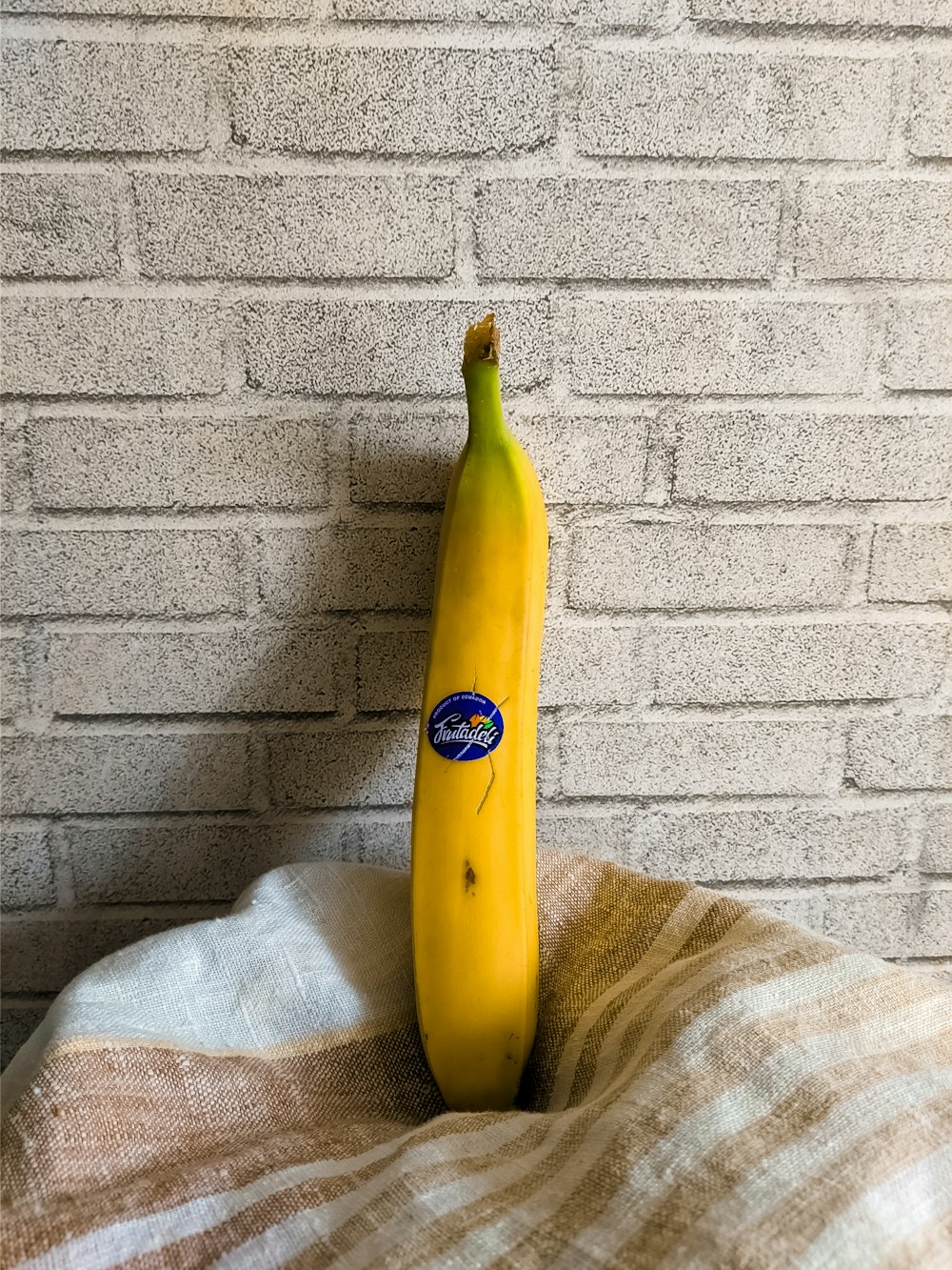 a banana sitting on top of a bed next to a brick wall