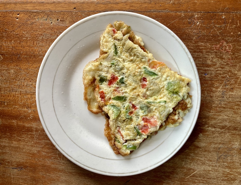 eine Scheibe Quiche auf einem weißen Teller auf einem Holztisch