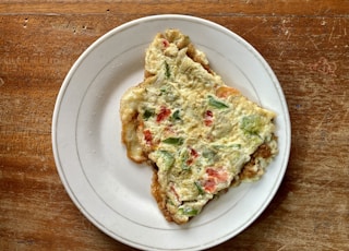 a slice of quiche on a white plate on a wooden table