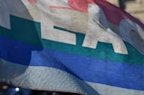 A colorful flag with the word 'PEACE' printed on it. The flag features horizontal stripes in red, yellow, green, and blue.