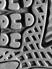 A close-up view of a textured surface, featuring a pattern of geometric shapes like circles and triangles. The material appears rubbery, with a detailed tread design suggesting it might be the sole of a shoe.